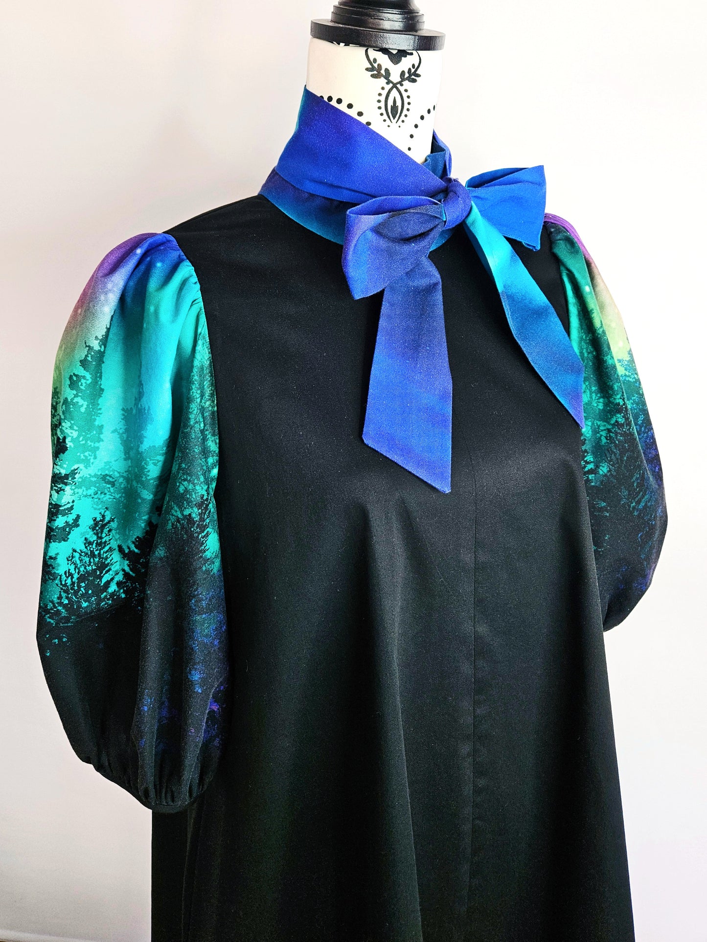 Black dress with colourful aurora print sleeves and blue bow on a mannequin against a white background