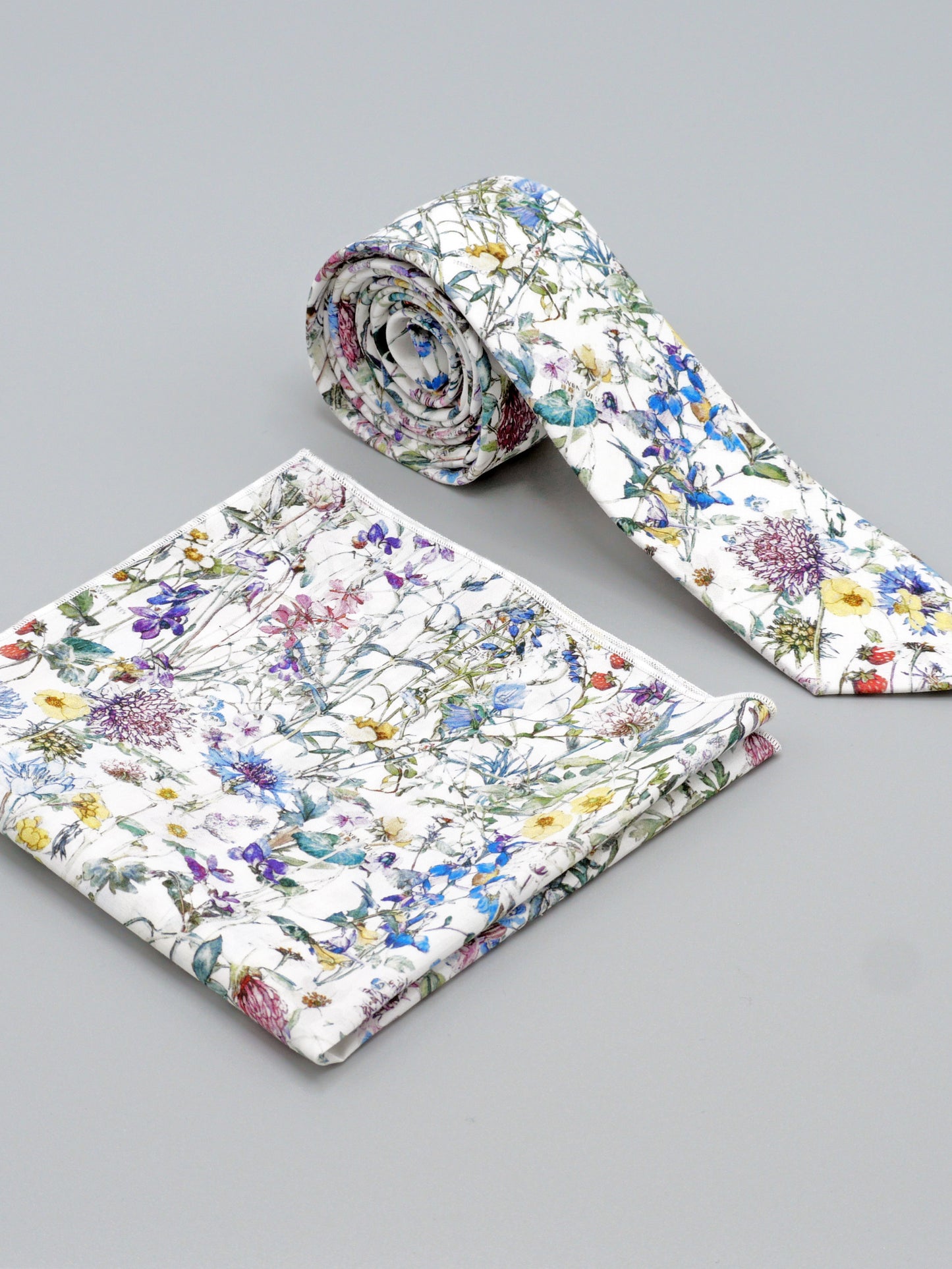Floral-patterned tie and a matching pocket square on a grey background