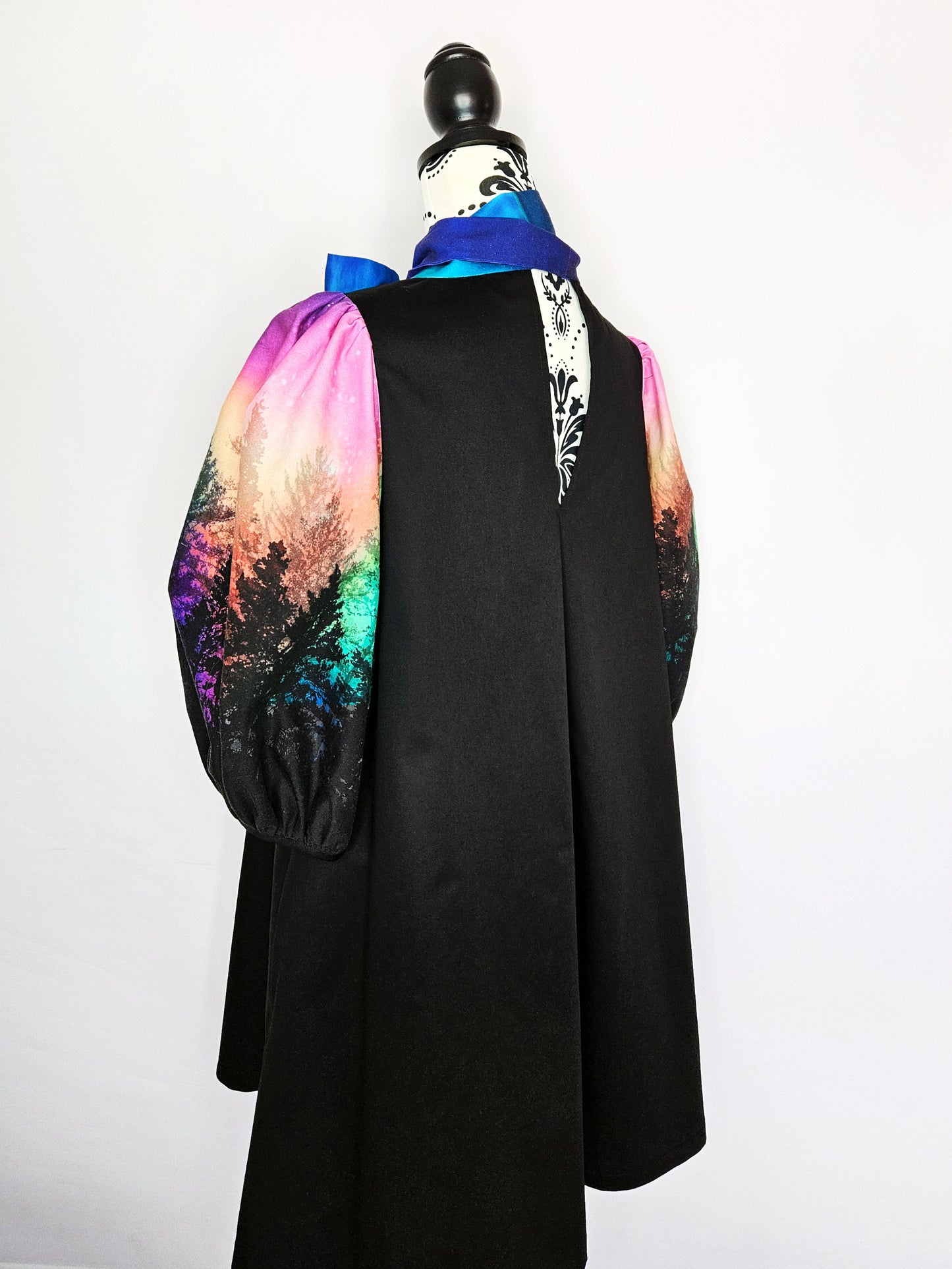Black dress with colourful aurora print sleeves and blue bow on a mannequin against a white background
