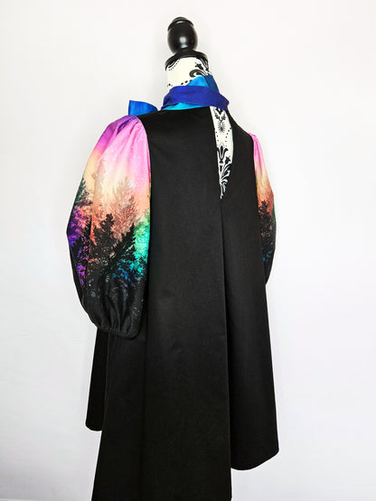 Black dress with colourful aurora print sleeves and blue bow on a mannequin against a white background