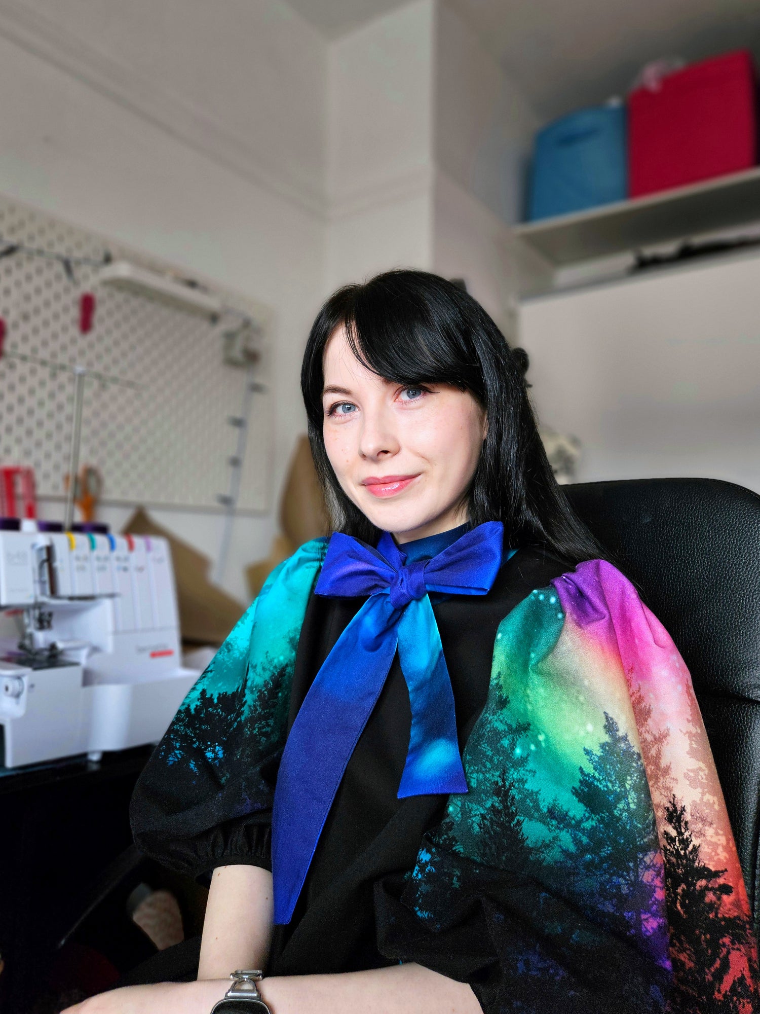 Woman wearing a black dress with colourful aurora print sleeves and a blue bow