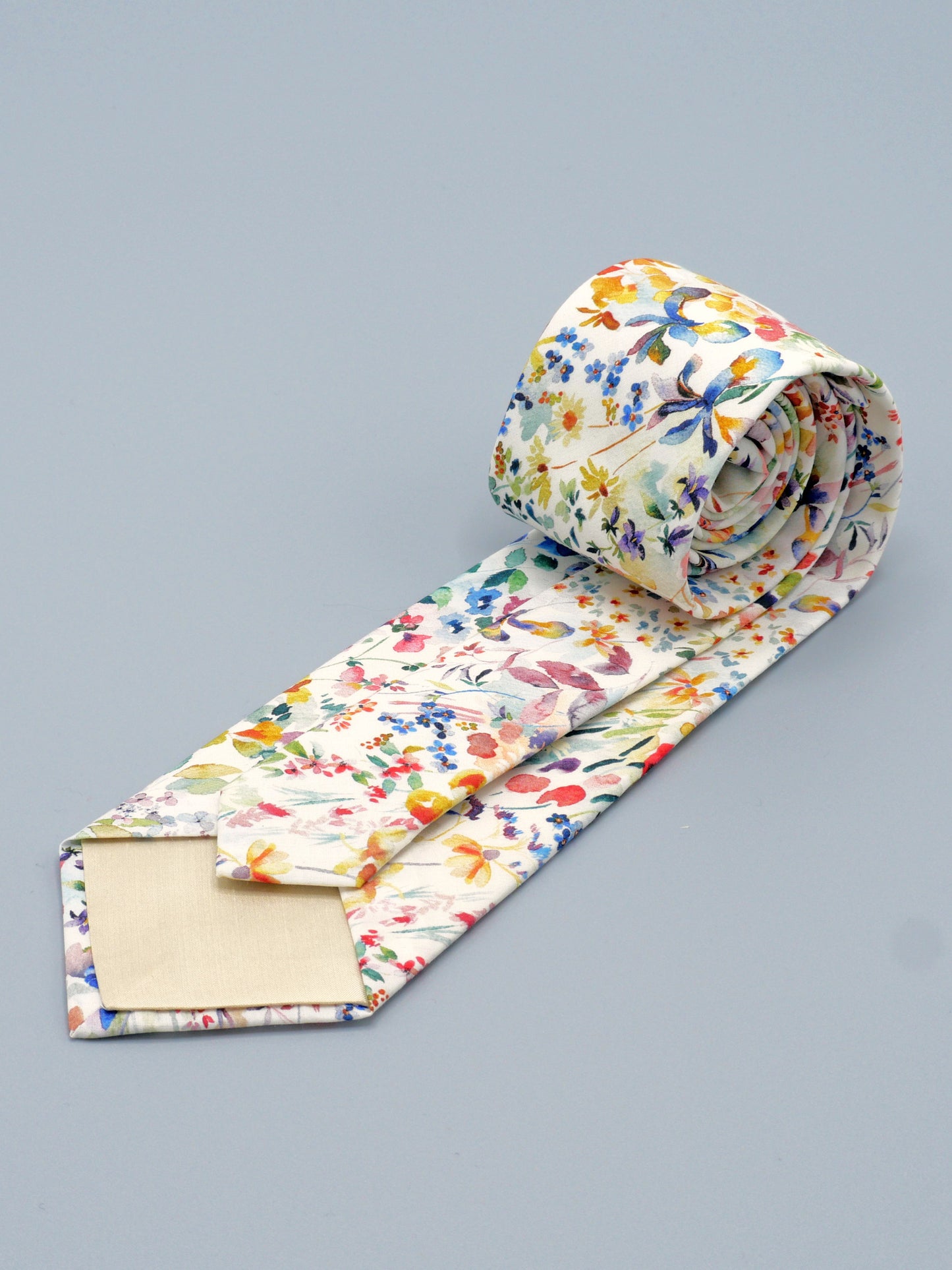 Floral watercolour style patterned tie rolled up on a grey background, with a cream lining