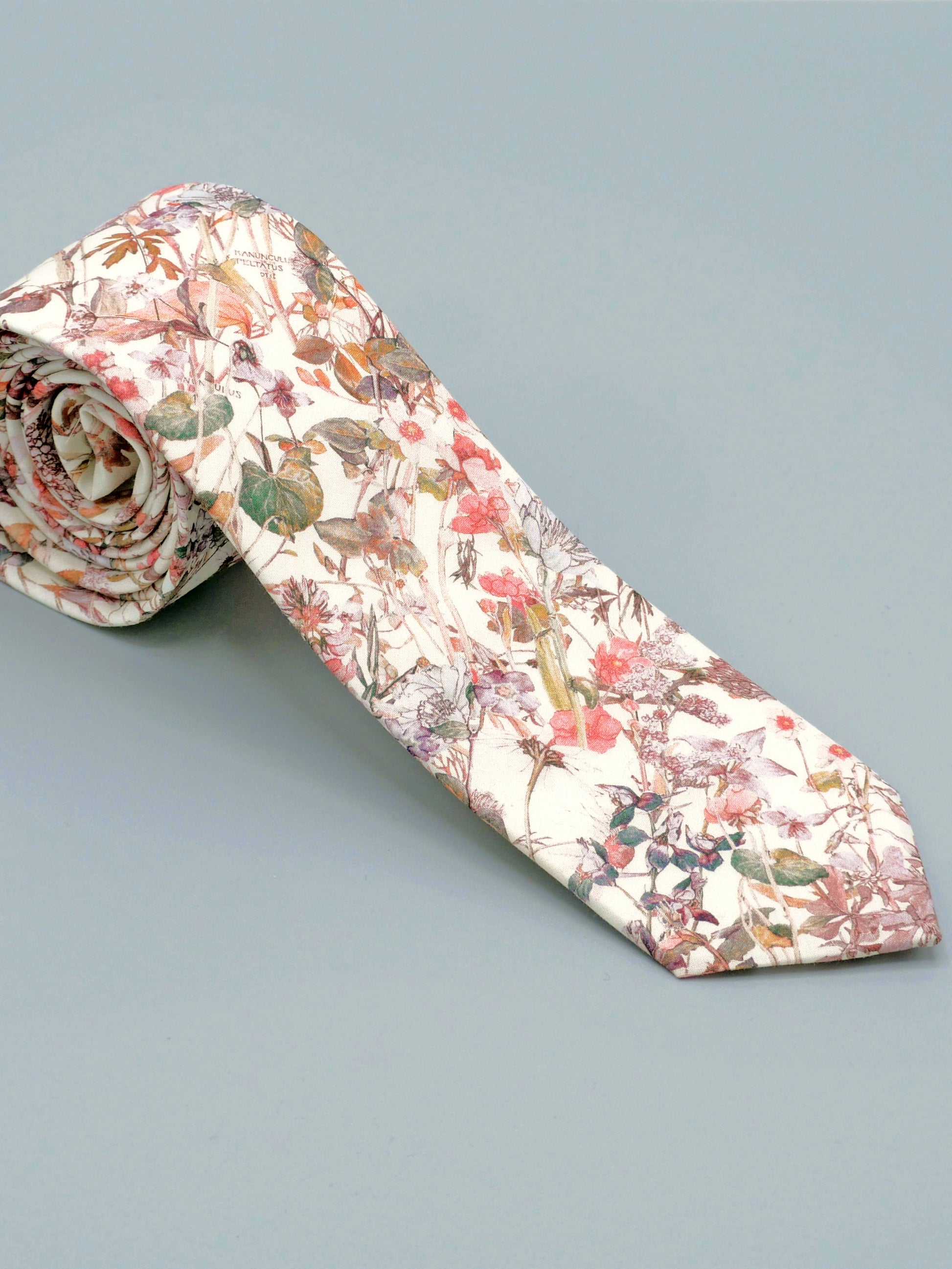 Floral patterned tie in a soft peach pink wildflower print rolled up on a light grey background