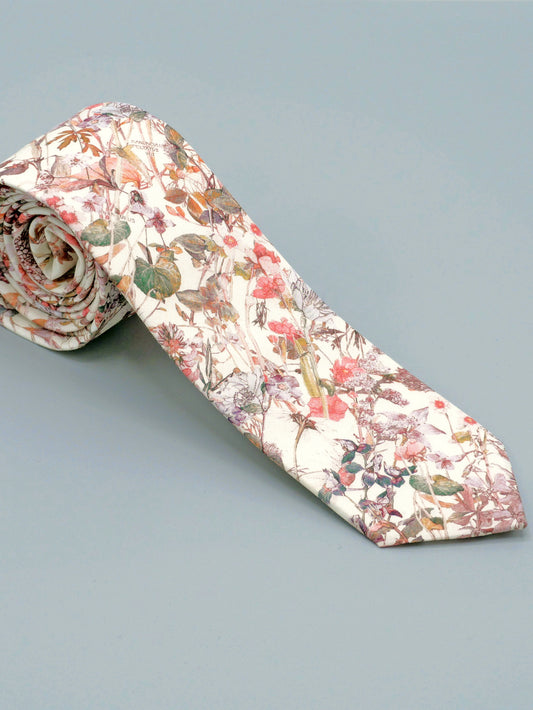 Floral patterned tie in a soft peach pink wildflower print rolled up on a light grey background