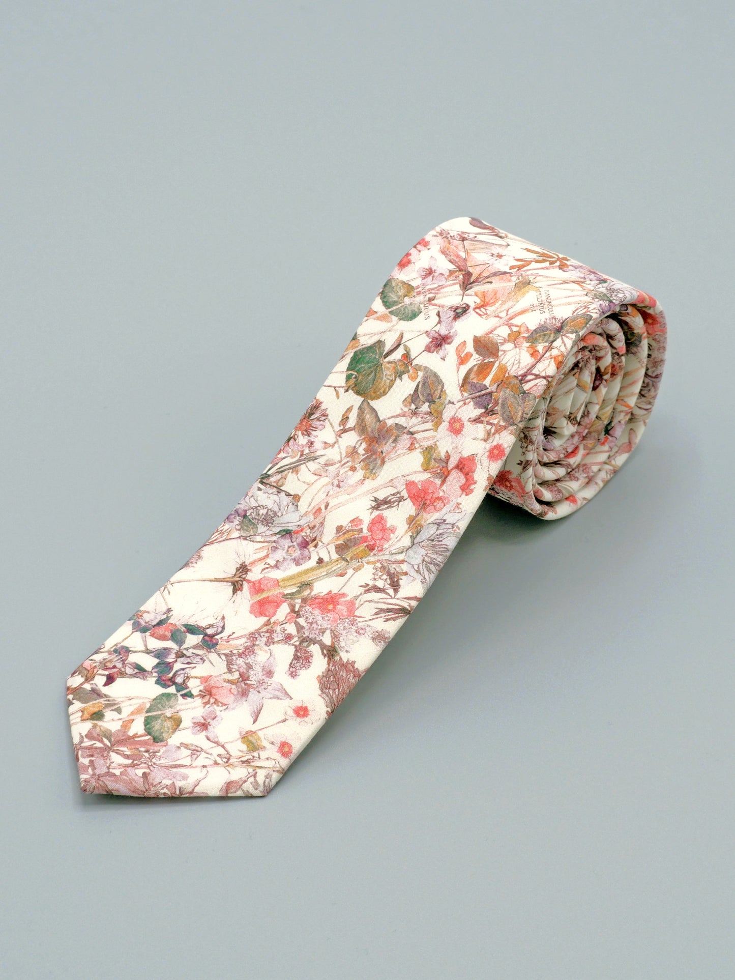 Floral patterned tie in a soft peach pink wildflower print rolled up on a light grey background