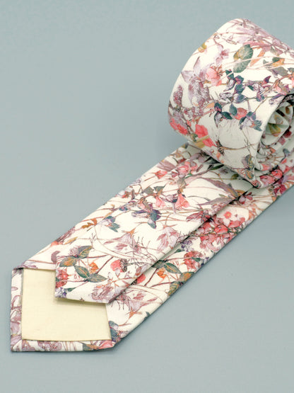 Floral patterned tie in a soft peach pink wildflower print and cream lining rolled up on a light grey background