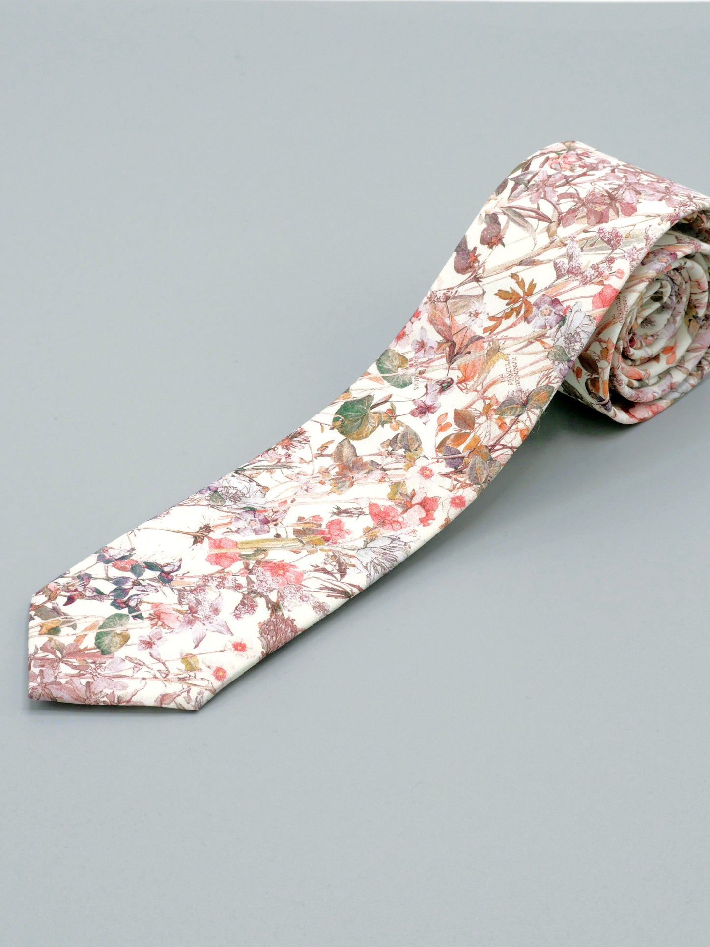 Floral patterned tie in a soft peach pink wildflower print rolled up on a light grey background