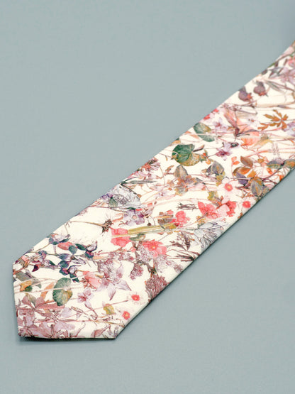 Floral patterned tie in a soft peach pink wildflower print lying flat on a light grey background