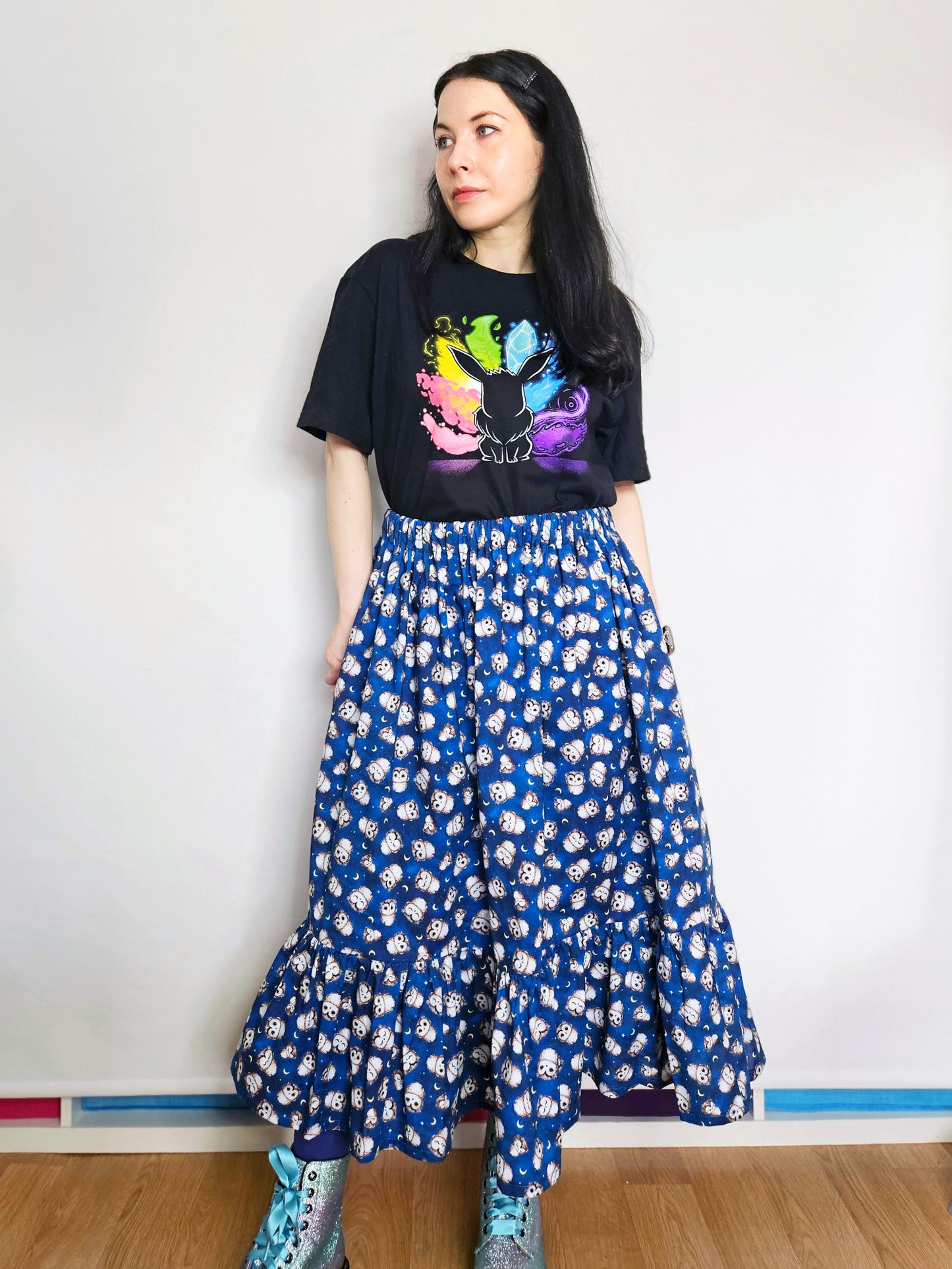 Person wearing a black t-shirt with colourful design and a blue owl print skirt