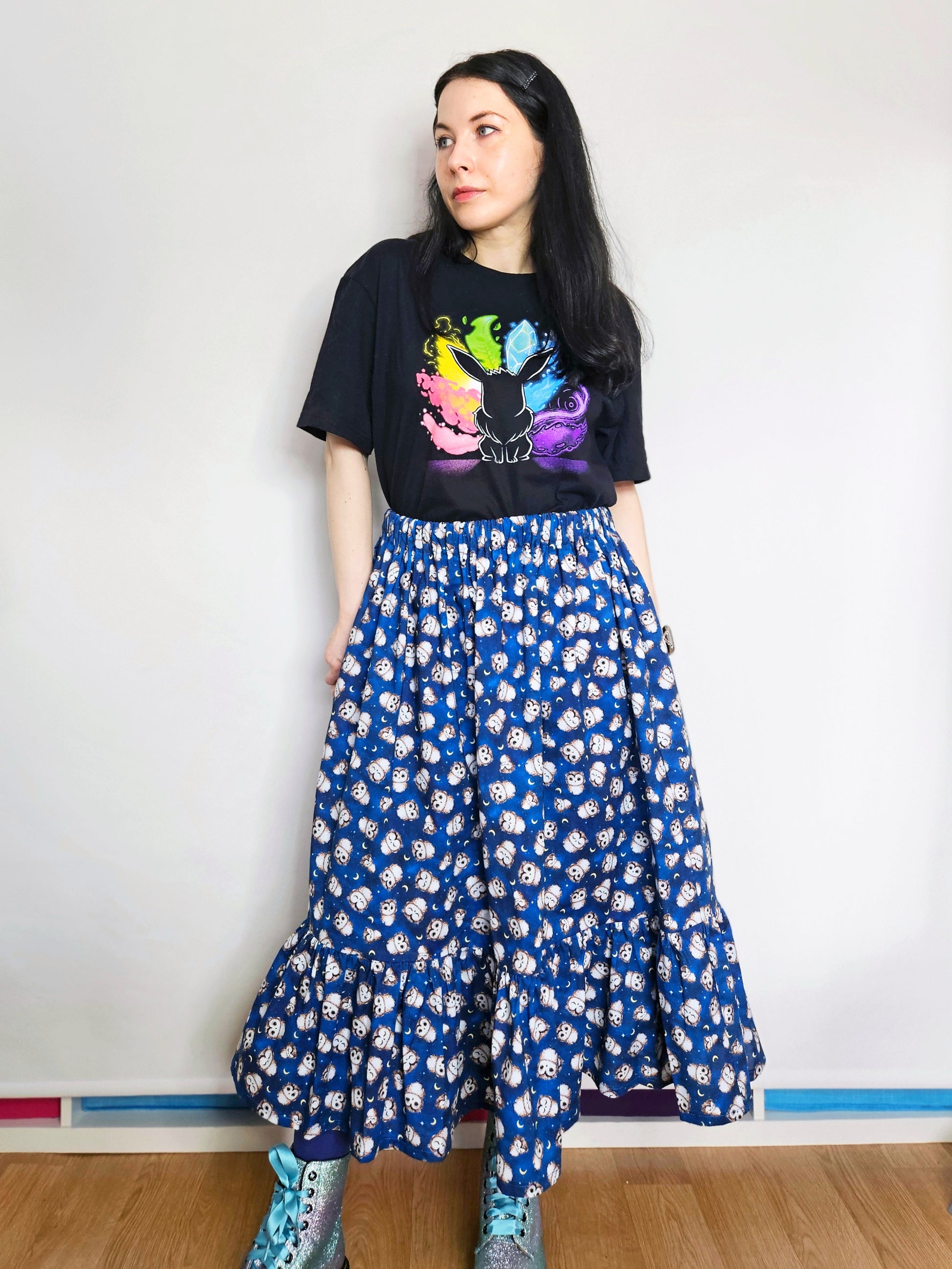 Person wearing a black t-shirt with colourful design and a blue owl print skirt
