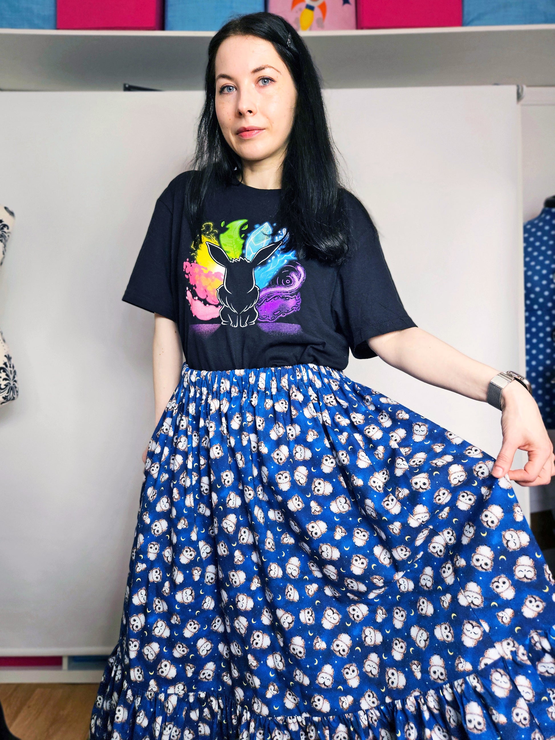 Person wearing a black t-shirt with colourful design and a blue owl print skirt