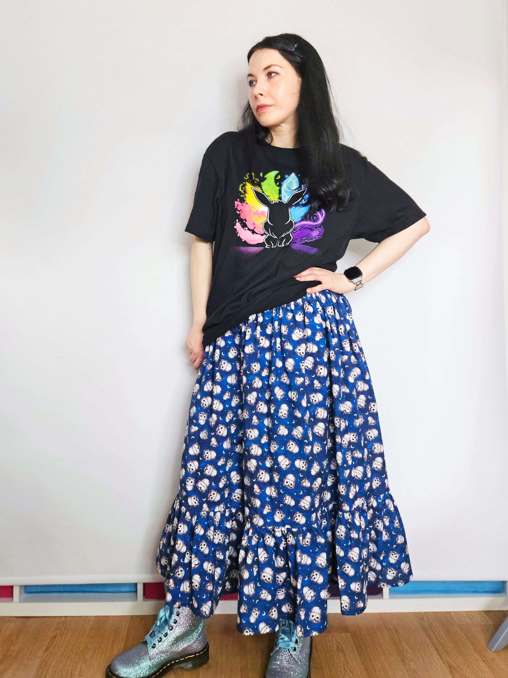 Person wearing a black t-shirt with colourful design and a blue owl print skirt