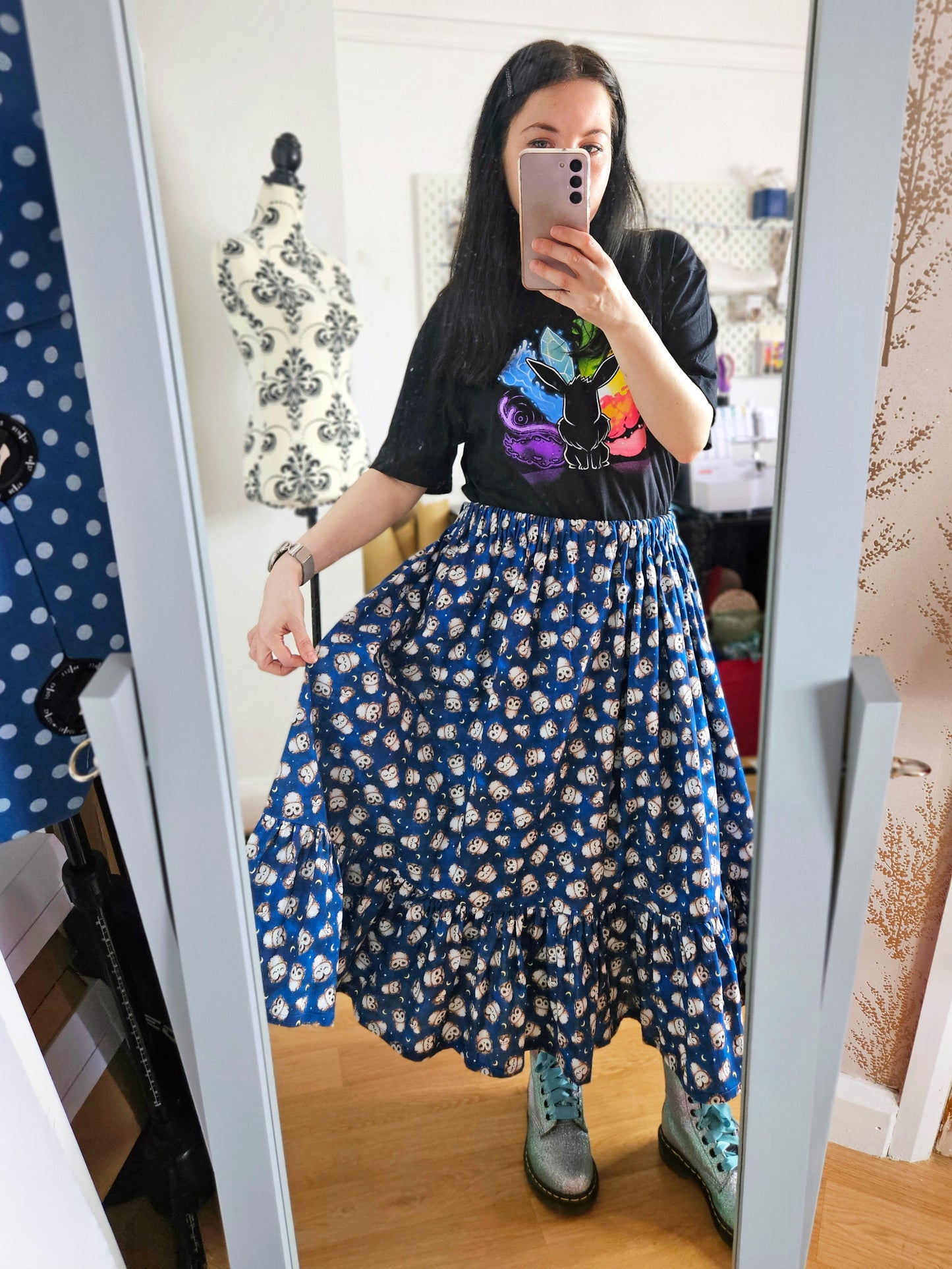 Person wearing a black t-shirt with colourful design and a blue owl print skirt