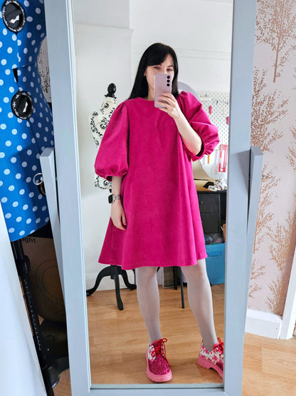 Person wearing a bright pink dress standing in front of a mirror.