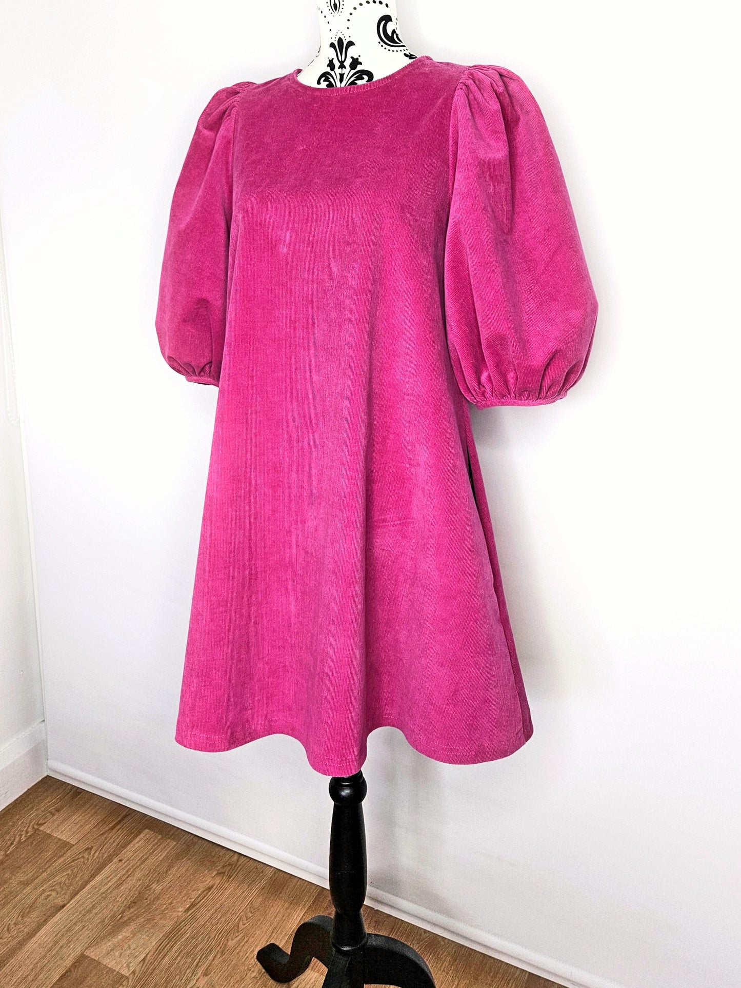 Bright pink dress with puff sleeves on a mannequin against a white wall.