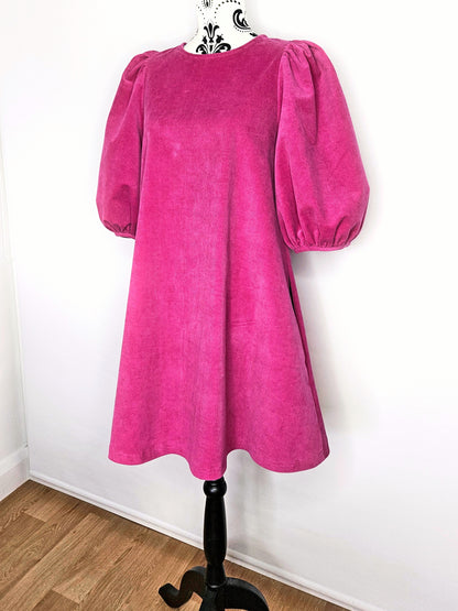 Bright pink dress with puff sleeves on a mannequin against a white wall.