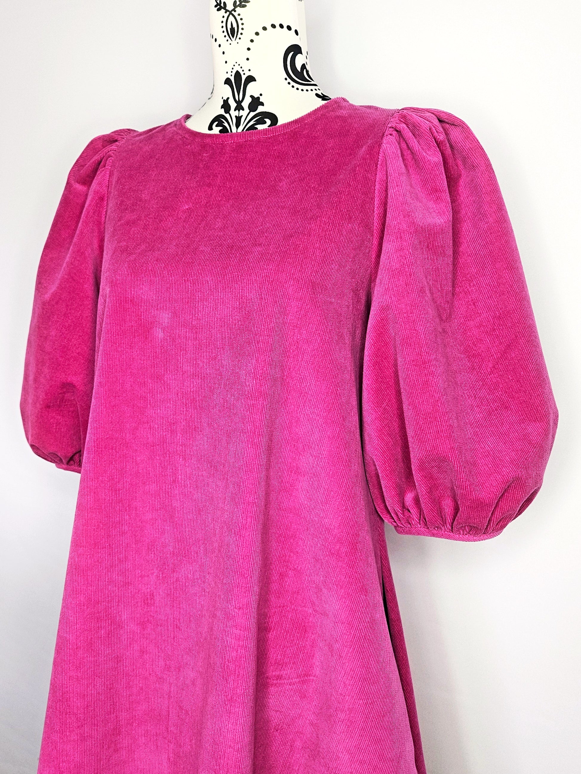 Bright pink dress with puff sleeves on a mannequin against a white wall.