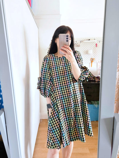 A woman takes a mirror selfie wearing a colourful pastel rainbow plaid dress with puff sleeves in a bright room.