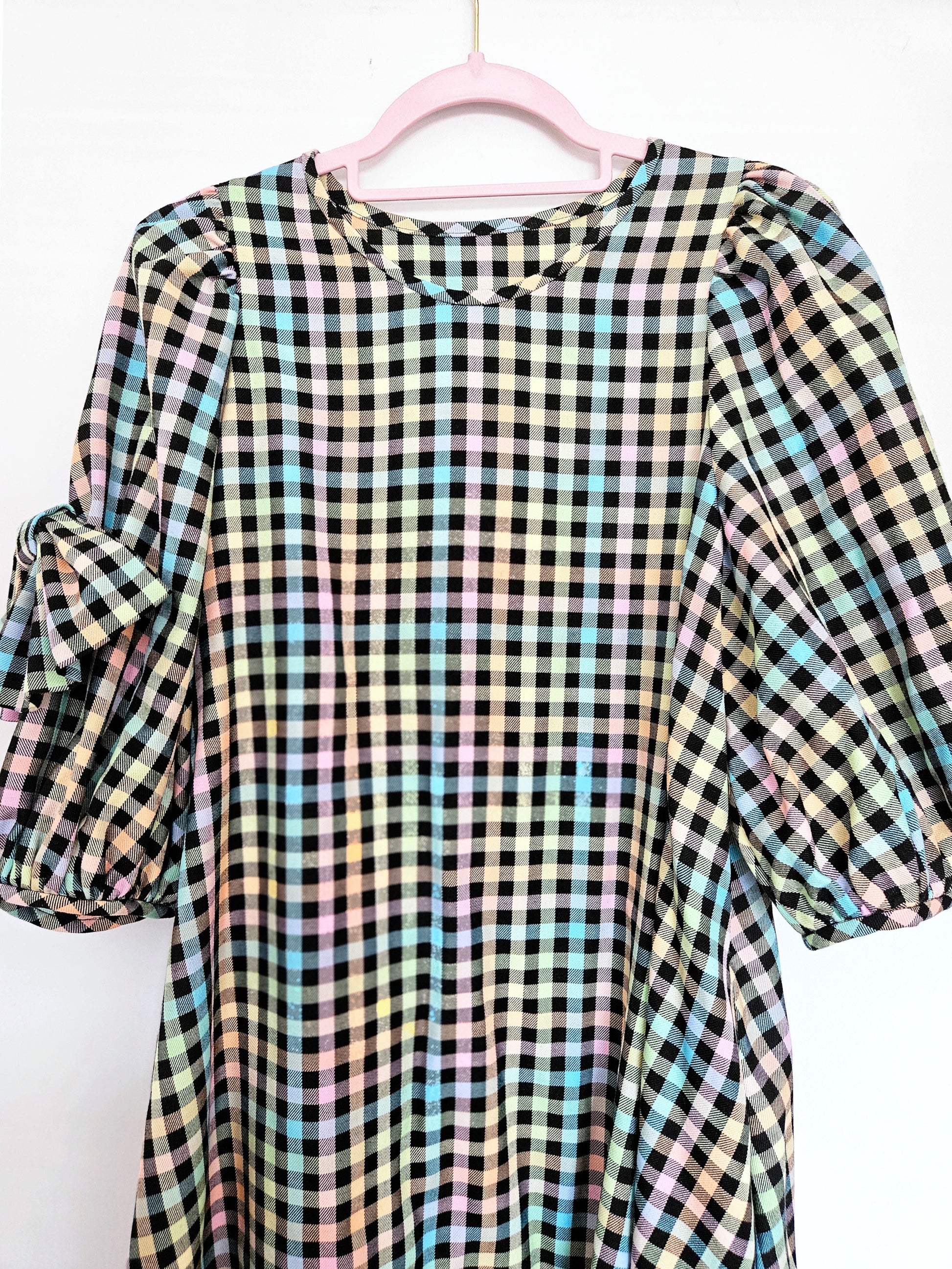 A multicolour pastel plaid dress with puff sleeves hanging on a pink hanger against a white background.