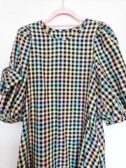A multicolour pastel plaid dress with puff sleeves hanging on a pink hanger against a white background.