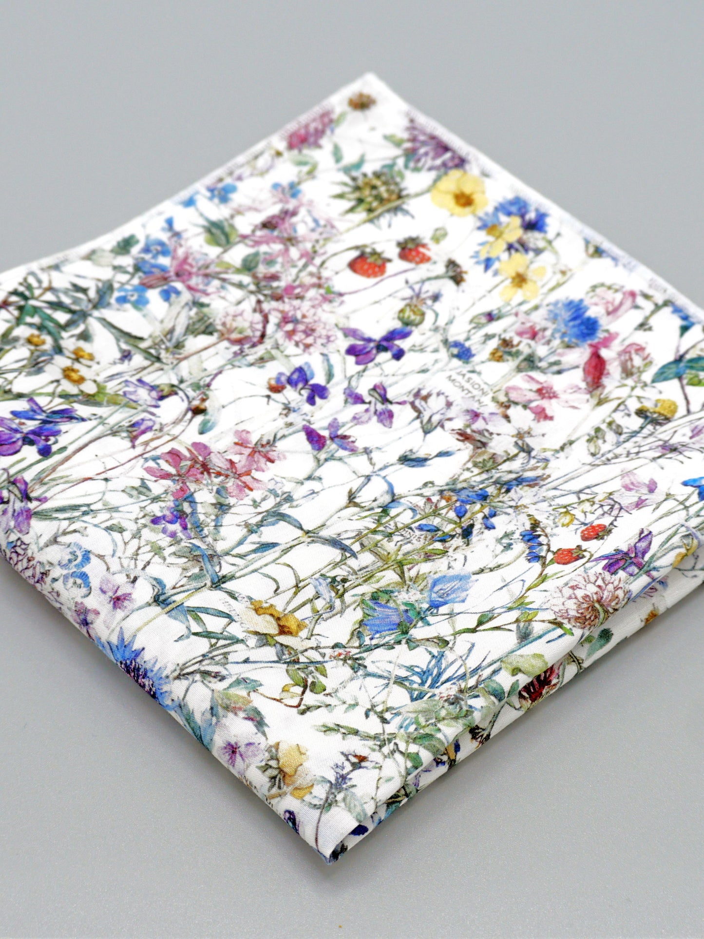 A close-up of a floral patterned pocket square on a grey background