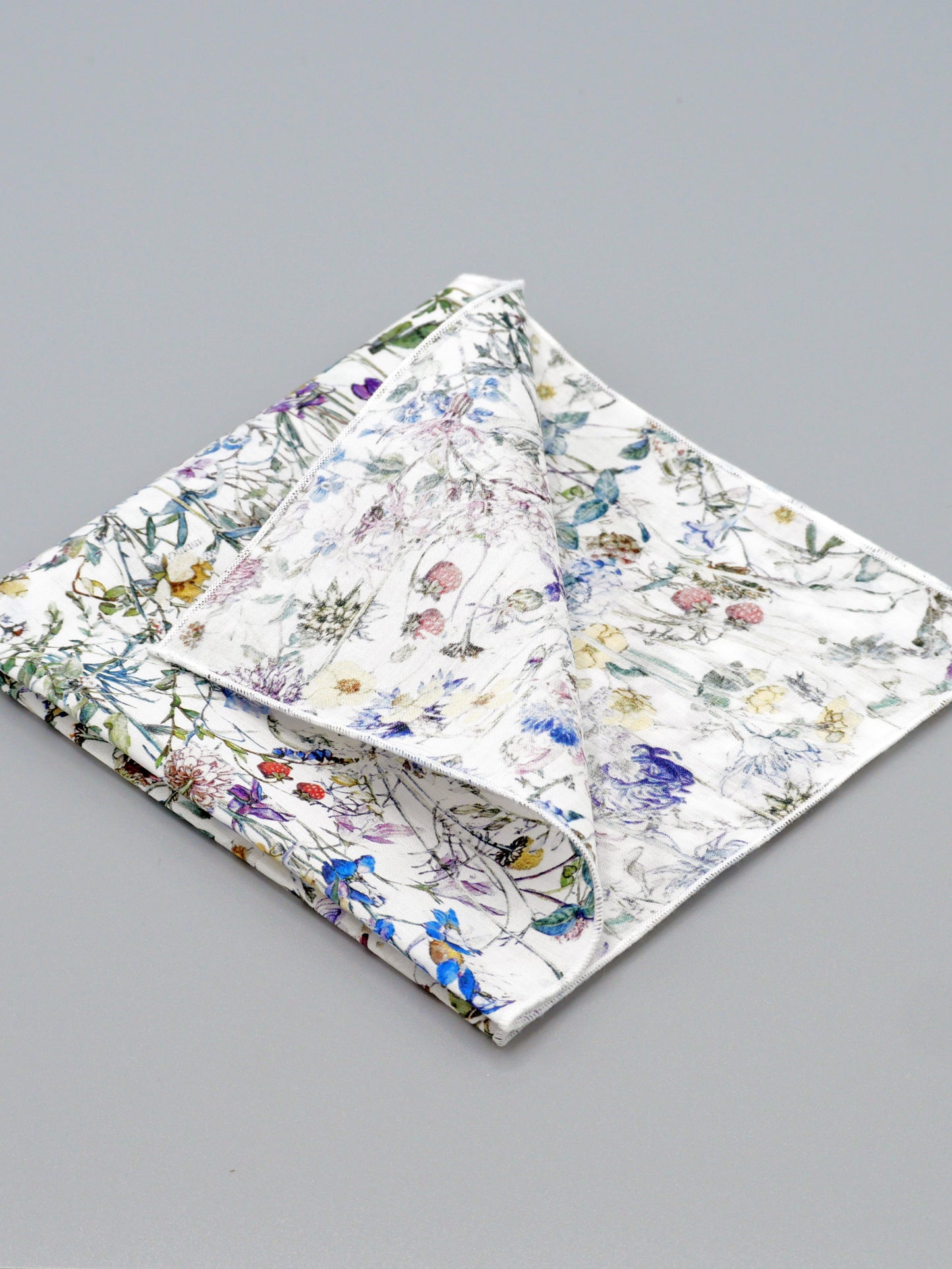 Floral patterned pocket square with a corner folded over on a grey background