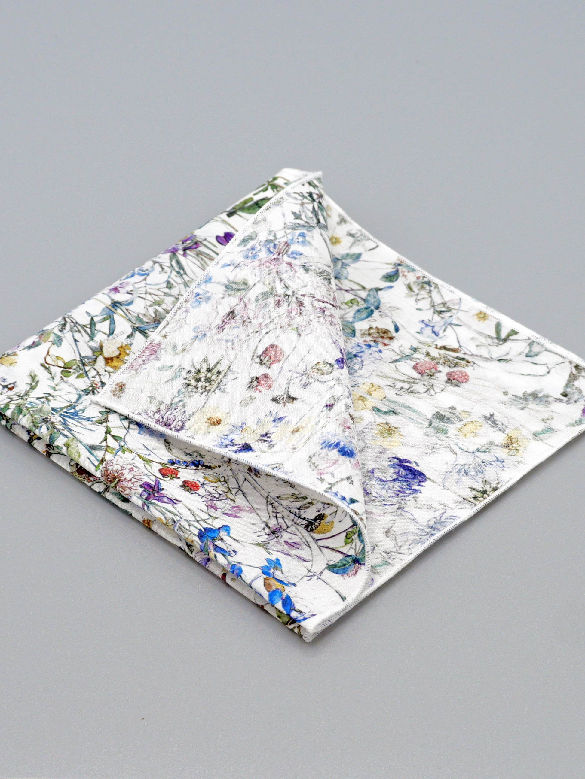 Floral patterned pocket square with a corner folded over on a grey background